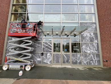 Two people on a construction lift apply decals to the front of a building
